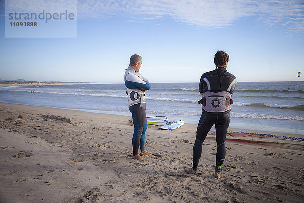 Zwei Surfer schauen auf das Meer und stehen am Strand