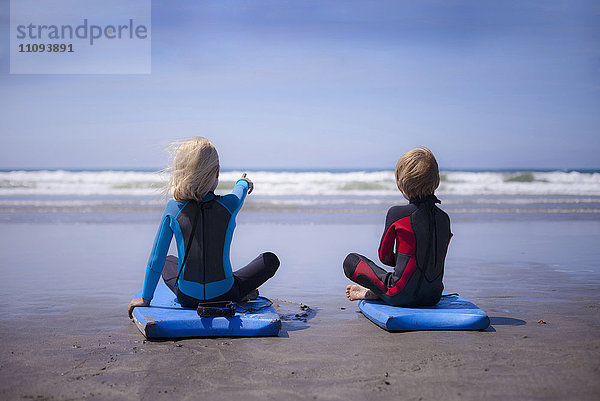 Rückansicht eines Mädchens  das ihrem Bruder am Strand etwas zeigt