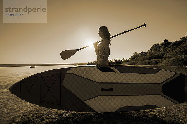 Ältere Frau mit Stand Up Paddle Board am Seeufer  Bayern  Deutschland