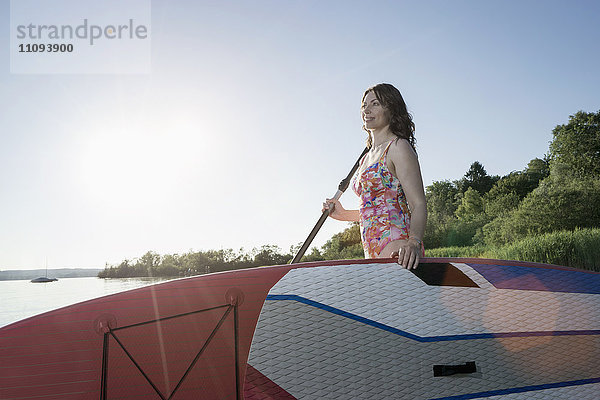 Ältere Frau mit Stand Up Paddle Board am Seeufer  Bayern  Deutschland