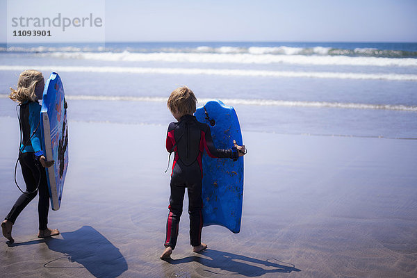 Zwei Geschwister halten Boogie Boarding am Strand