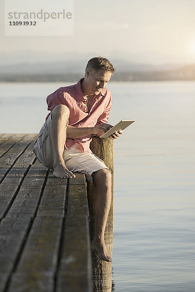 Älterer Mann  der ein digitales Tablet auf einem Seeufer benutzt  Bayern  Deutschland
