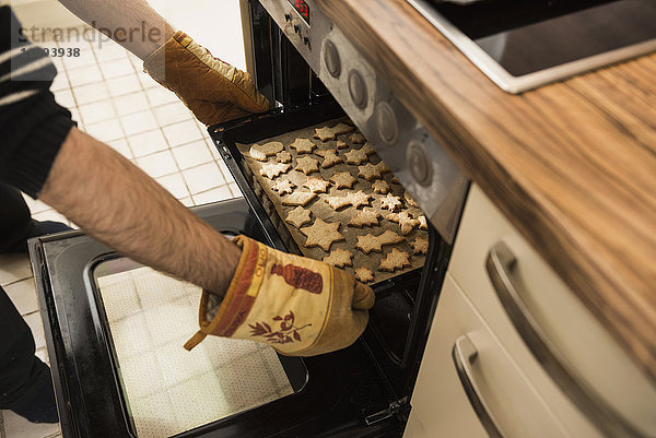 Nahaufnahme eines Mannes  der gebackene Kekse aus dem Ofen nimmt