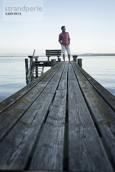 Älterer Mann steht auf einem Holzsteg und schaut in die Ferne  Bayern  Deutschland