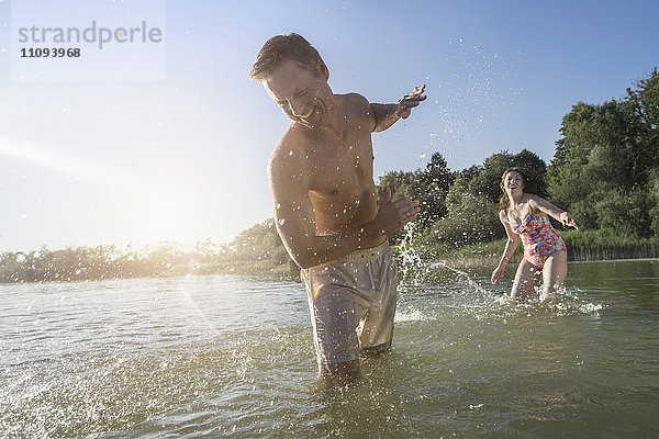 Reife Frau bespritzt ihren Mann am See mit Wasser  Bayern  Deutschland