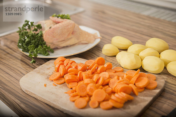 Geschnittene Karotten  geschälte Kartoffeln  rohes Hühnerfleisch mit Petersilie am Küchentisch