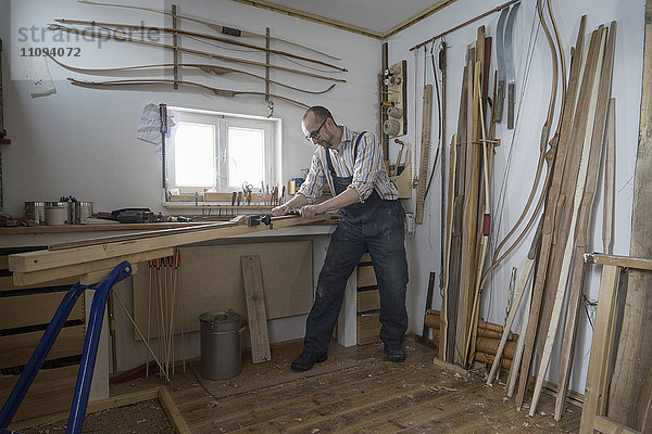 Männlicher Bogenbauer  der Holz spaltet und es in Form eines Bogens bringt  in einer Werkstatt  Bayern  Deutschland