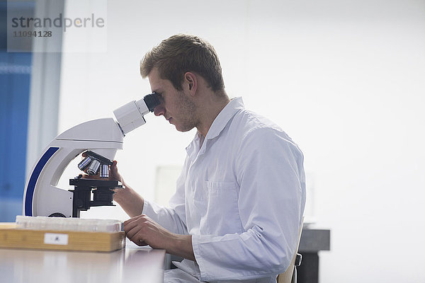 Junger männlicher Wissenschaftler schaut durch ein Mikroskop in einem Hörsaal