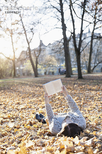 Ältere Frau liest ein Buch im Liegen auf gefallenen Blättern im Park  Bayern  Deutschland