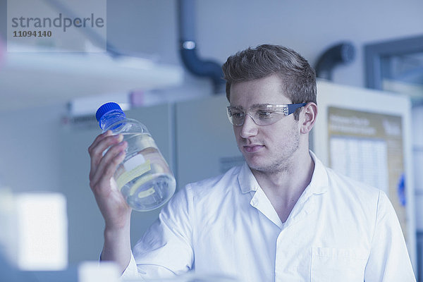 Junger männlicher Wissenschaftler hält Flüssigkeitsflasche in einem Apothekenlabor