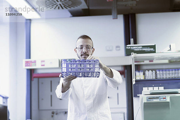 Junge Wissenschaftlerin ordnet Reagenzgläser in einem Reagenzglasgestell im Apothekenlabor an