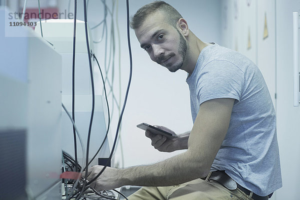 Männlicher Ingenieur hält ein digitales Tablet und repariert ein Gerät im Labor