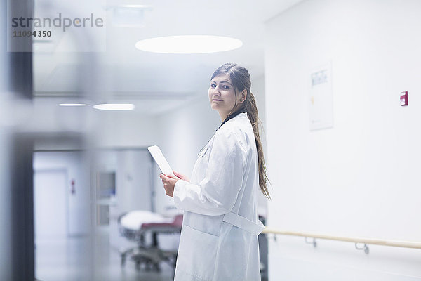 Junge Ärztin  die ein digitales Tablet in einem Krankenhauskorridor benutzt