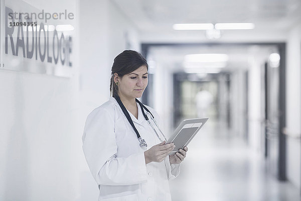 Junge Ärztin  die ein digitales Tablet in einem Krankenhauskorridor benutzt