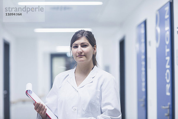 Porträt einer jungen Ärztin mit Klemmbrett in einem Krankenhauskorridor
