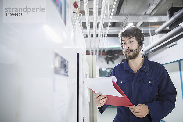 Junger männlicher Ingenieur  der ein Headset trägt und in einer Industrieanlage arbeitet