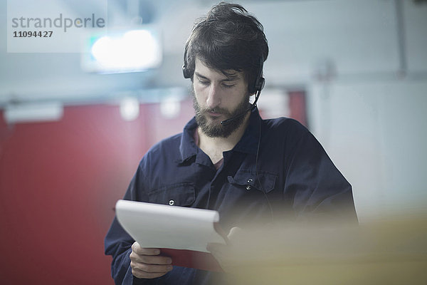 Junger männlicher Ingenieur  der ein Headset trägt und in einer Industrieanlage arbeitet