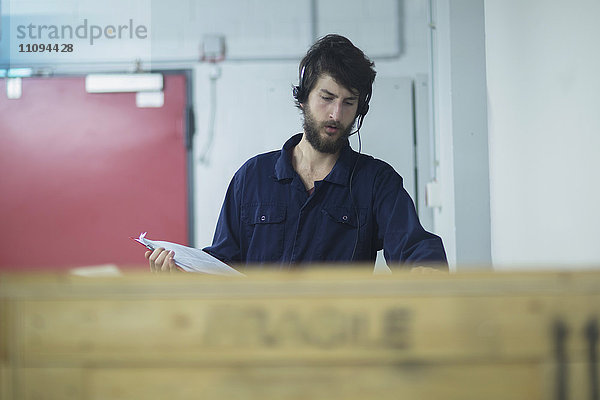 Junger männlicher Ingenieur  der ein Headset trägt und einen Frachtcontainer in einer Industrieanlage überprüft