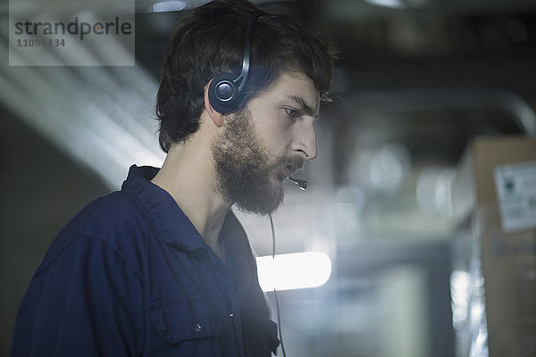 Junger männlicher Ingenieur  der ein Headset trägt und in einer Industrieanlage arbeitet