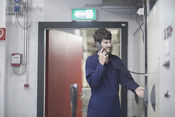 Junger männlicher Ingenieur im Gespräch am Festnetztelefon in einer Industrieanlage