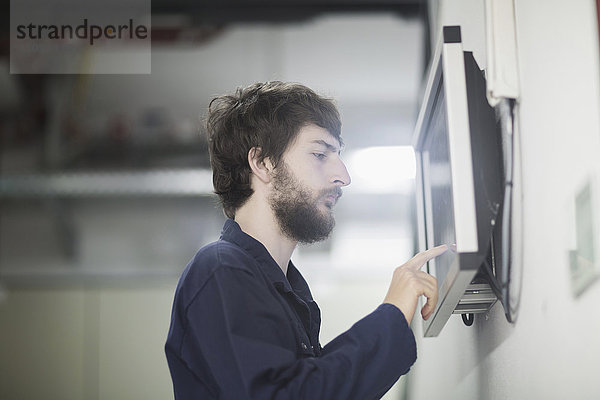 Junger männlicher Ingenieur bei der Arbeit an einem Touchscreen-Computermonitor in einer Industrieanlage