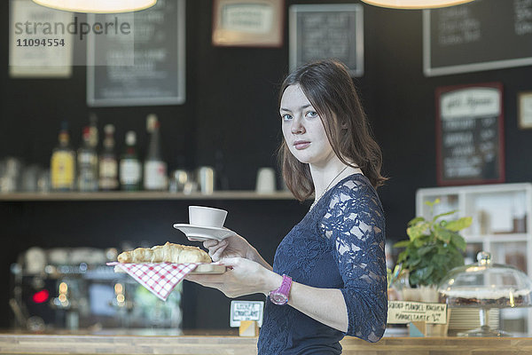 Junge Kellnerin serviert Kaffee und Croissant in einem Kaffeehaus