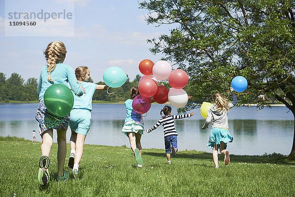 Rückansicht von Mädchen  die im Park mit Luftballons laufen  Karlsfelder See  München  Bayern  Deutschland