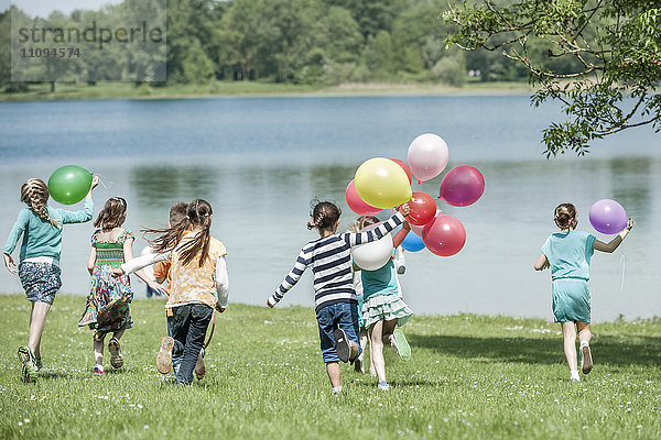 Rückansicht von Kindern  die im Park mit Luftballons laufen  München  Bayern  Deutschland