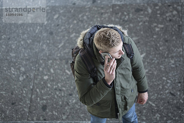 Blick von oben auf einen jungen Mann  der mit einem Mobiltelefon spricht