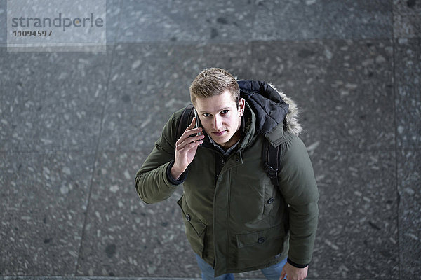 Blick von oben auf einen jungen Mann  der mit einem Mobiltelefon spricht