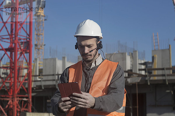 Junger männlicher Ingenieur benutzt ein digitales Tablet auf einer Baustelle