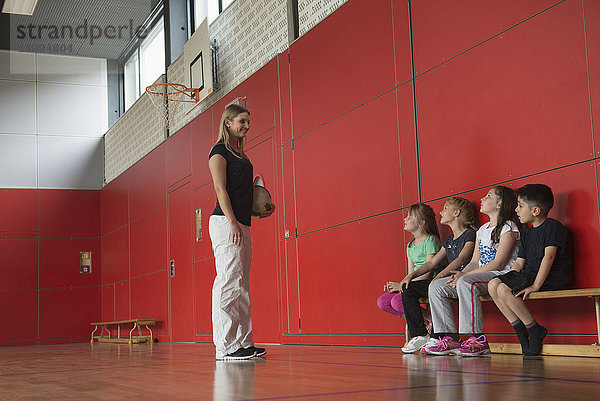 Lehrer gibt Kindern in einer Sporthalle Tipps für ein Gruppenspiel  München  Deutschland  Bayern