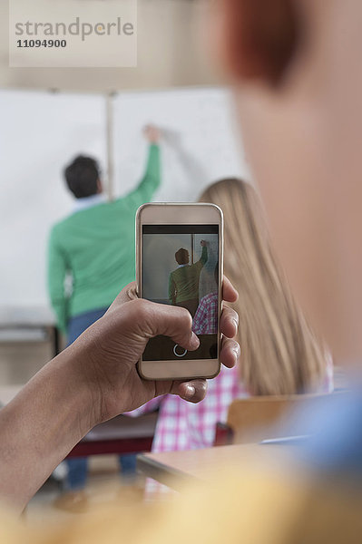 Lehrer unterrichtet im Klassenzimmer  während Schüler mit ihrem Smartphone ein Foto von ihm machen  Bayern  Deutschland