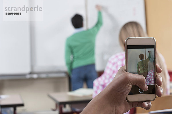 Lehrer unterrichtet im Klassenzimmer  während Schüler mit ihrem Smartphone ein Foto von ihm machen  Bayern  Deutschland