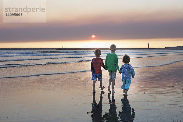 Rückansicht von drei Kindern  die bei Sonnenuntergang am Strand spazieren gehen  Viana do Castelo  Region Norte  Portugal