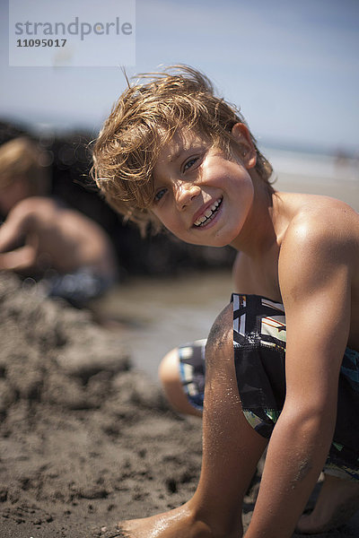 Porträt eines Jungen  der eine Sandburg baut und am Strand lächelt  Viana do Castelo  Region Norte  Portugal