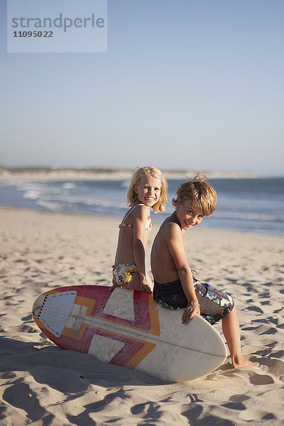 Zwei Kinder sitzen auf einem Bodyboard am Strand  Viana do Castelo  Region Norte  Portugal