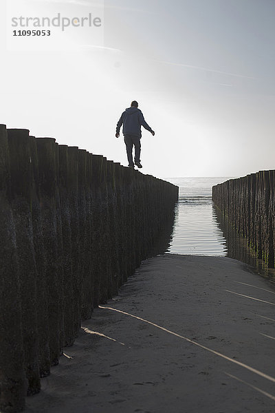 Silhouette eines reifen Mannes  der auf einem Holzpfosten am Strand balanciert  Renesse  Schouwen-Duiveland  Zeeland  Niederlande