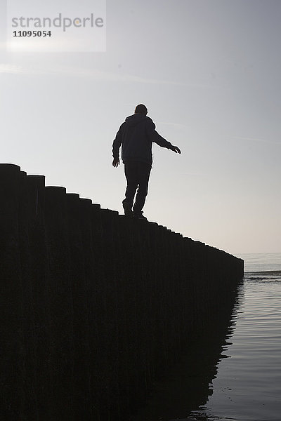 Silhouette eines reifen Mannes  der auf einem Holzpfosten am Strand balanciert  Renesse  Schouwen-Duiveland  Zeeland  Niederlande