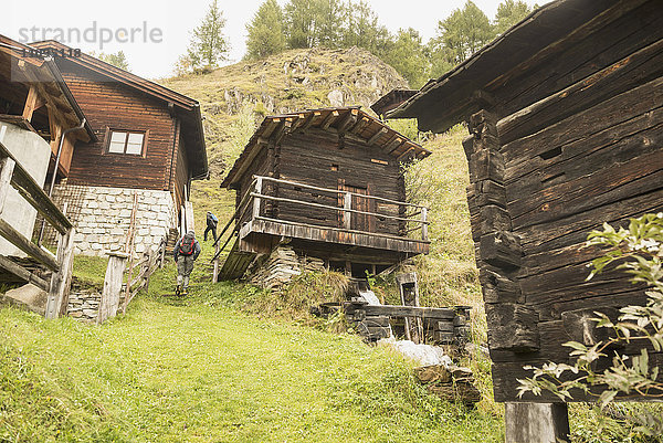 Rückansicht zweier erwachsener Wanderer  die an Hütten vorbeigehen  Österreichische Alpen  Kärnten  Österreich