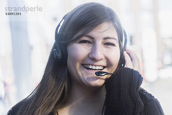 Porträt einer lächelnden jungen Frau  die über ein Headset spricht  Freiburg im Breisgau  Baden-Württemberg  Deutschland