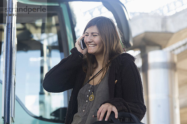 Junge Frau  die mit einem Mobiltelefon spricht und vor einem Bus steht  Freiburg im Breisgau  Baden-Württemberg  Deutschland