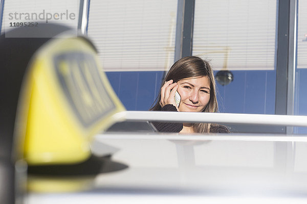 Junge Frau  die hinter einem Taxi mit einem Mobiltelefon spricht  Freiburg im Breisgau  Baden-Württemberg  Deutschland