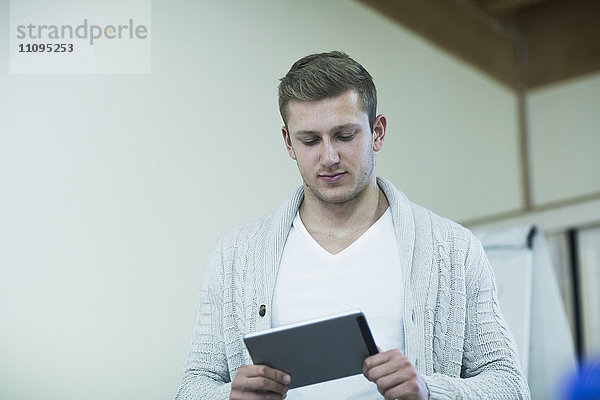 Junger männlicher Lehrer bei der Arbeit an einem digitalen Tablet im Klassenzimmer  Freiburg im Breisgau  Baden-Württemberg  Deutschland