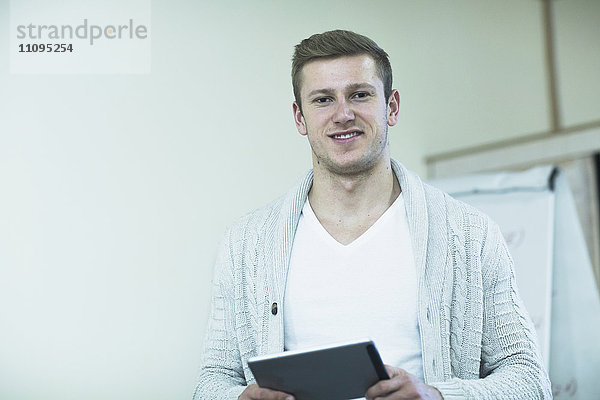 Junger männlicher Lehrer bei der Arbeit an einem digitalen Tablet im Klassenzimmer  Freiburg im Breisgau  Baden-Württemberg  Deutschland