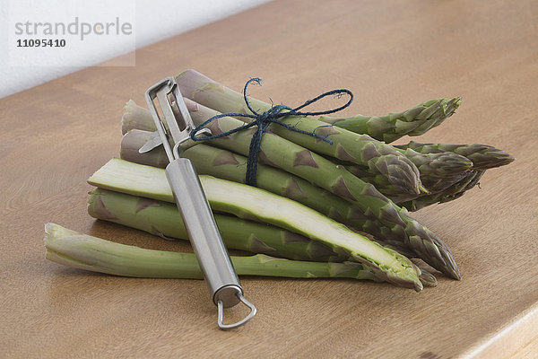 Bündel grüner Spargel mit Schälmaschine auf dem Tisch