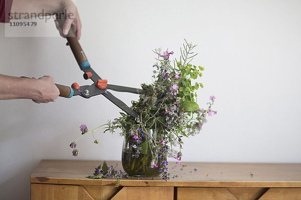 Frustrierte Frau  die eine Vasenblume mit einer Gartenschere schneidet