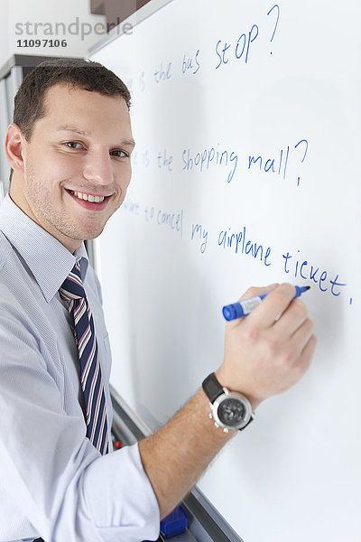 Junger männlicher Lehrer schreibt am Whiteboard