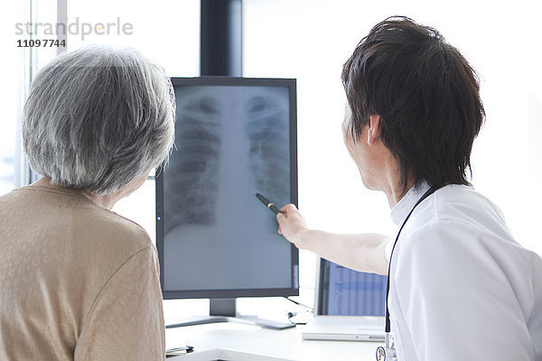 Arzt betrachtet Röntgenbild mit älterer Frau