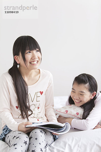 Zwei Teenager-Mädchen auf dem Bett mit Blick auf Magazin